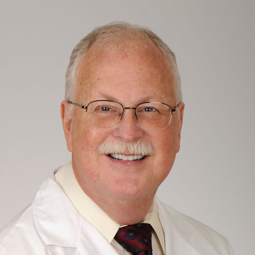 a dentist at charlotte dental arts smiling wearing glasses and a suit