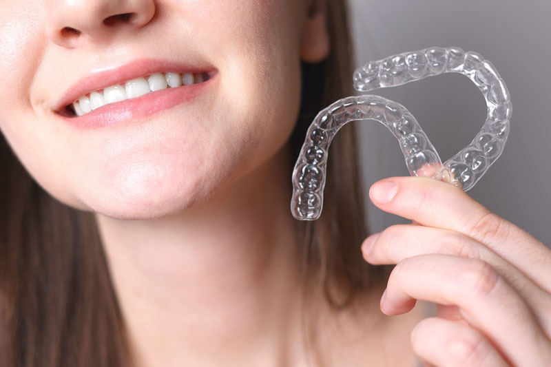 a woman smiling with straight teeth and an Invisalign retainer in her hand